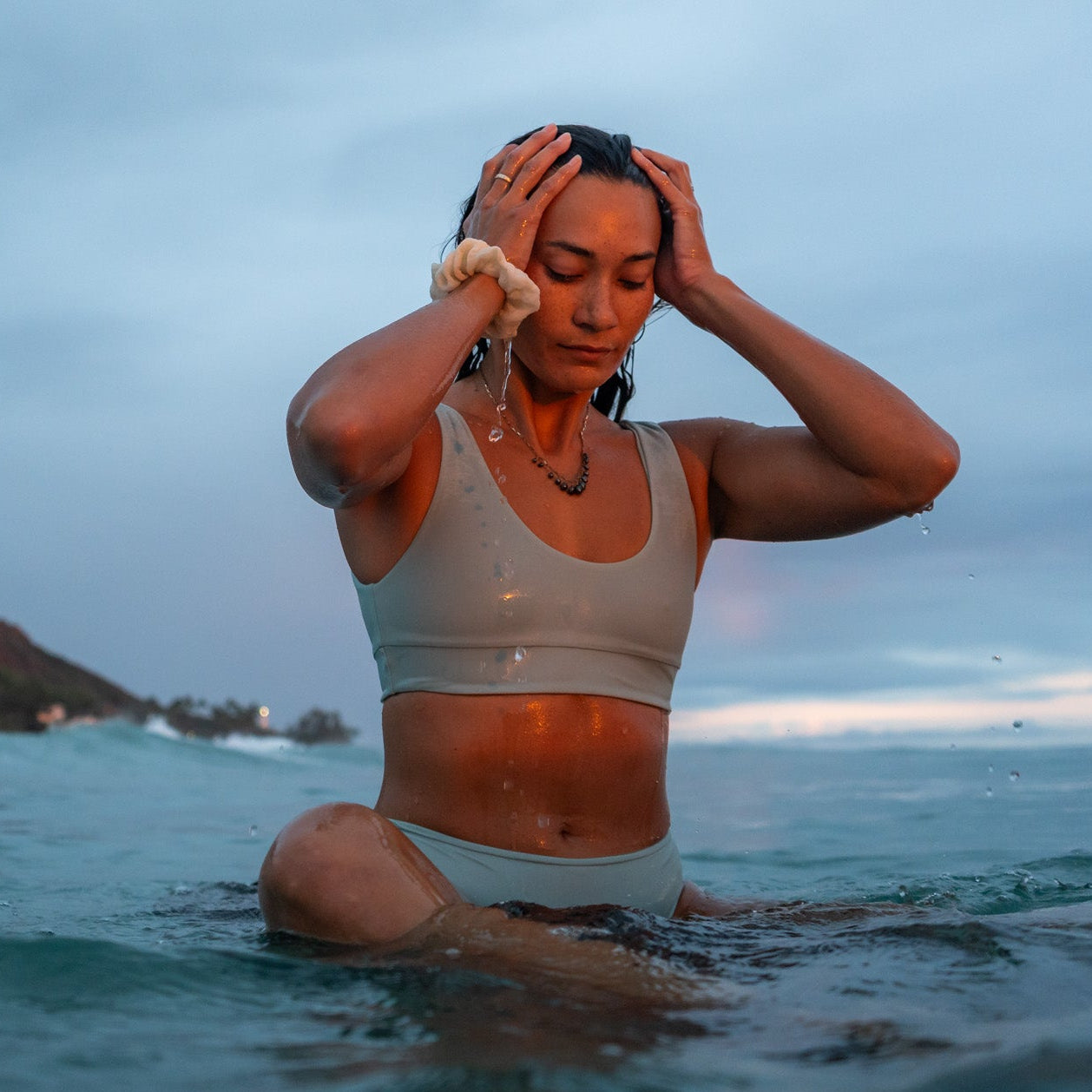 Person in a swimsuit sitting in the ocean with a mountainous landscape in the background