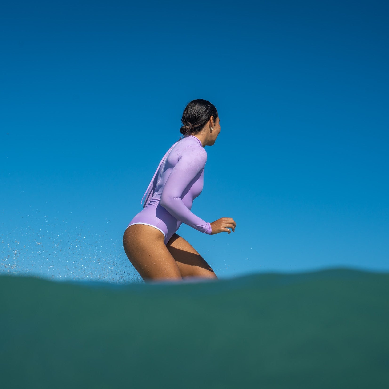 A woman surfing in a purple long sleeve surf suit behind a wave