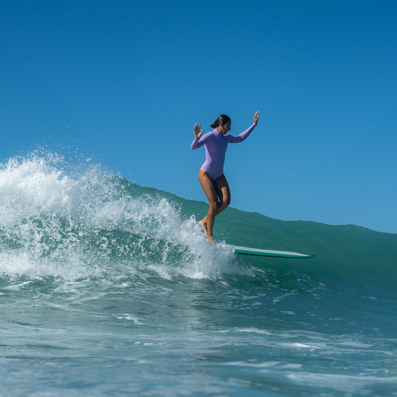 Person surfing on a wave in a purple long sleeve swimsuit
