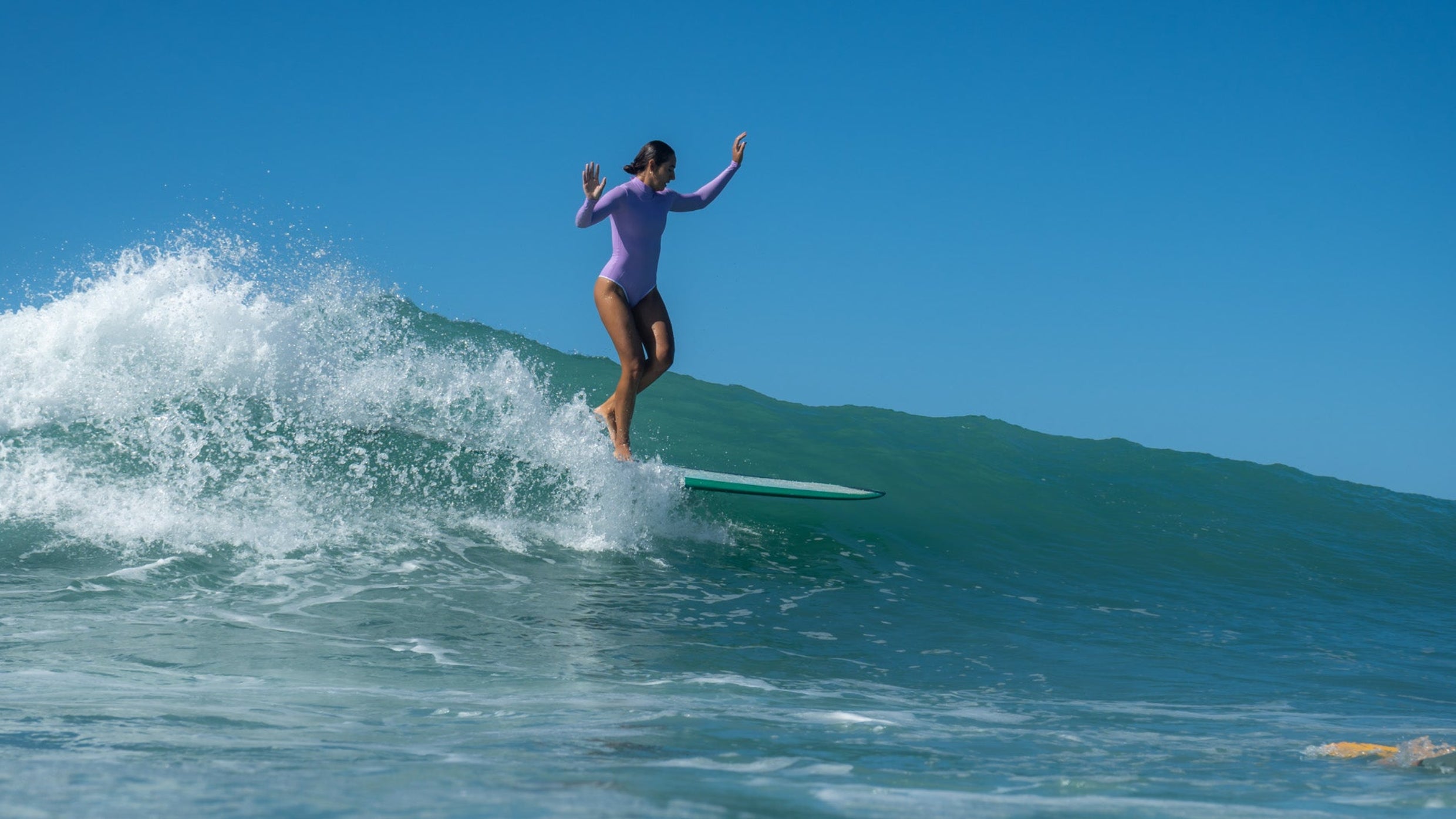 Person surfing on a wave with another surfer in the water.