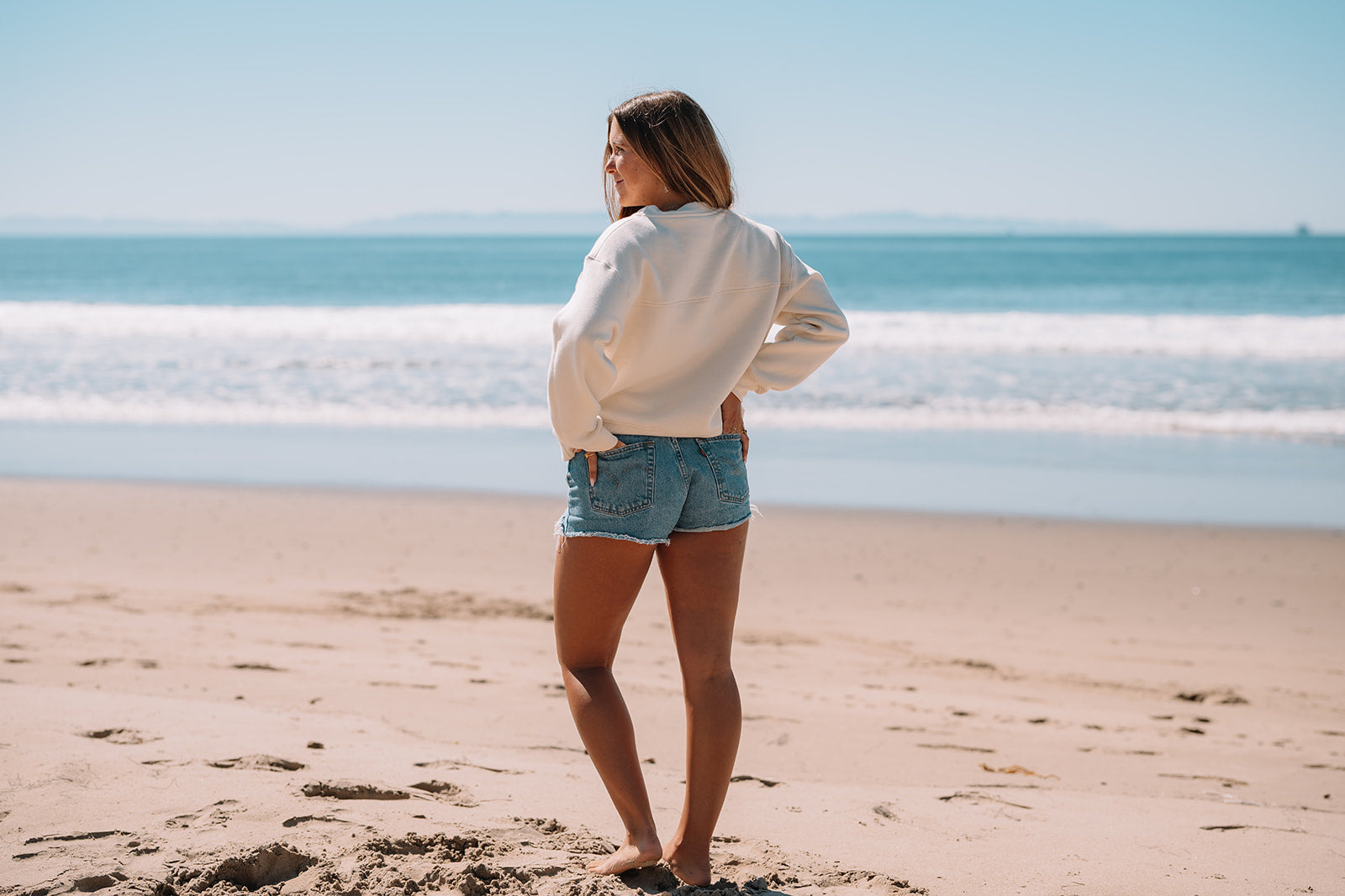 Girl in white sweatshirt with hands on hips in front of ocean