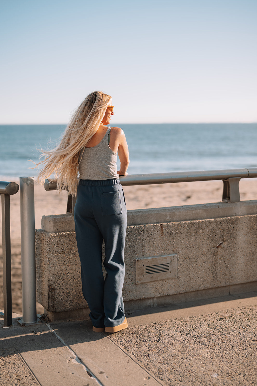 Woman standing by a railing overlooking the ocean on a sunny day.