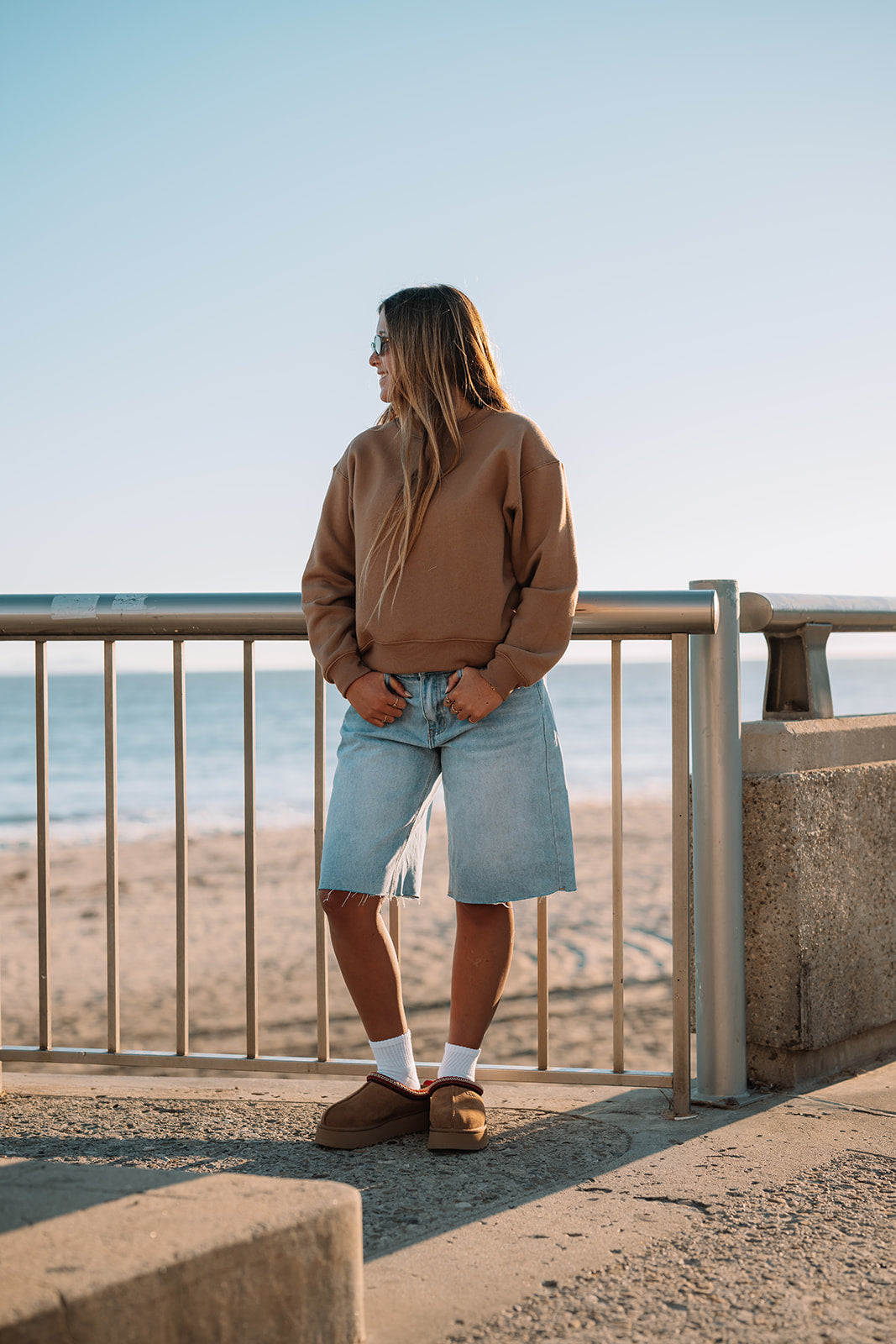 Person standing by a railing overlooking a beach with a clear sky.