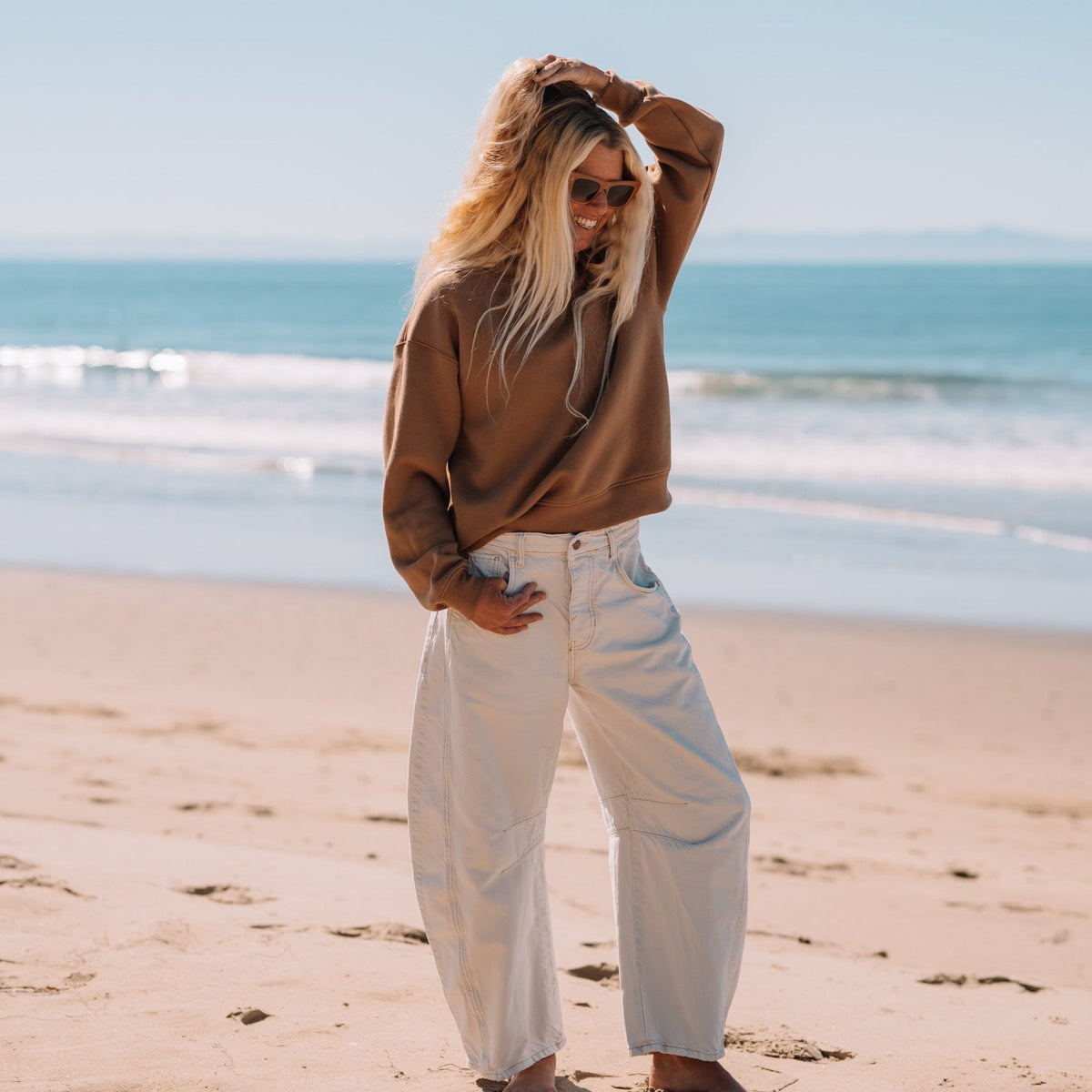 Woman standing on a beach with a brown sweatshirt near the ocean 