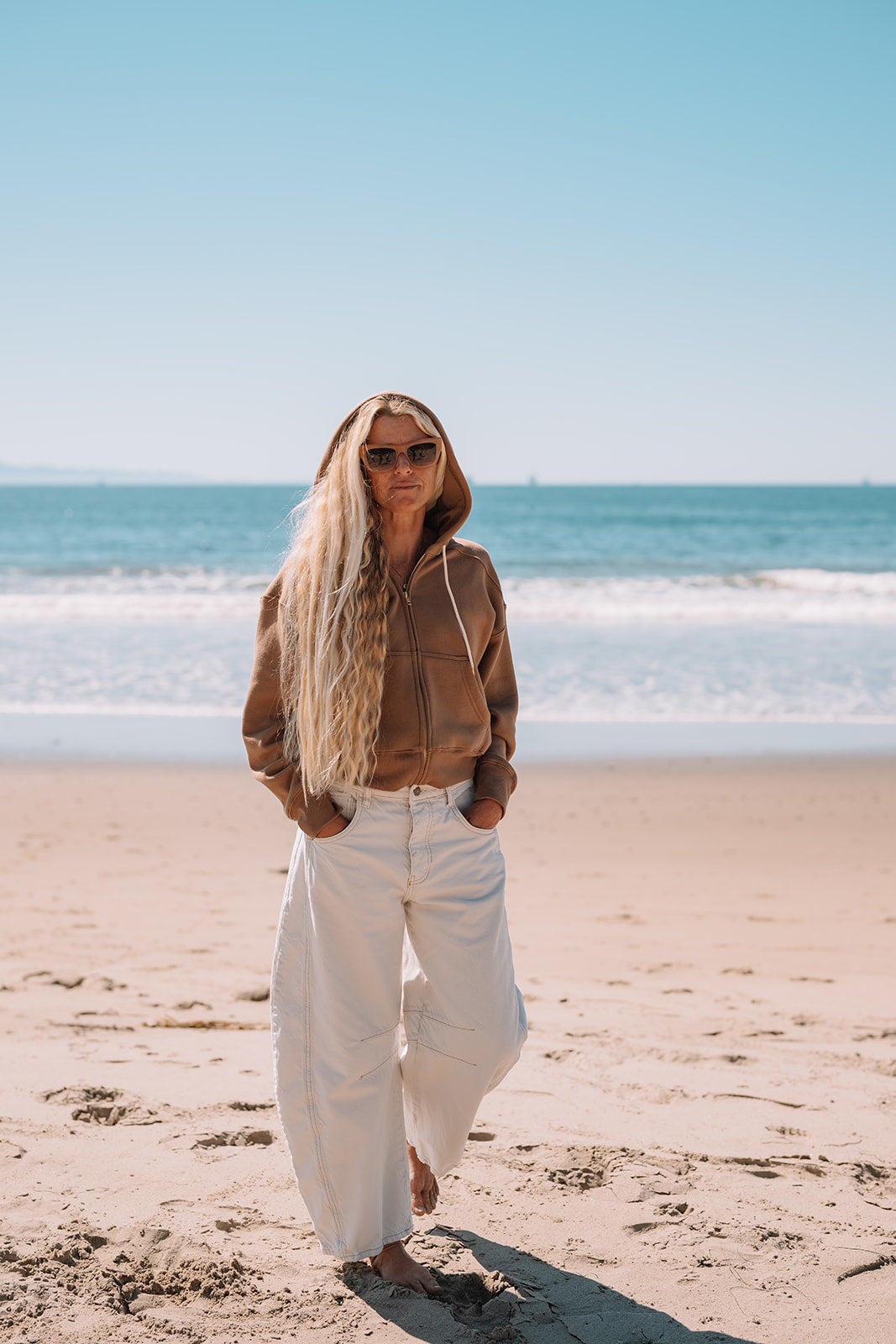 Woman standing on a beach wearing sunglasses and casual clothing.