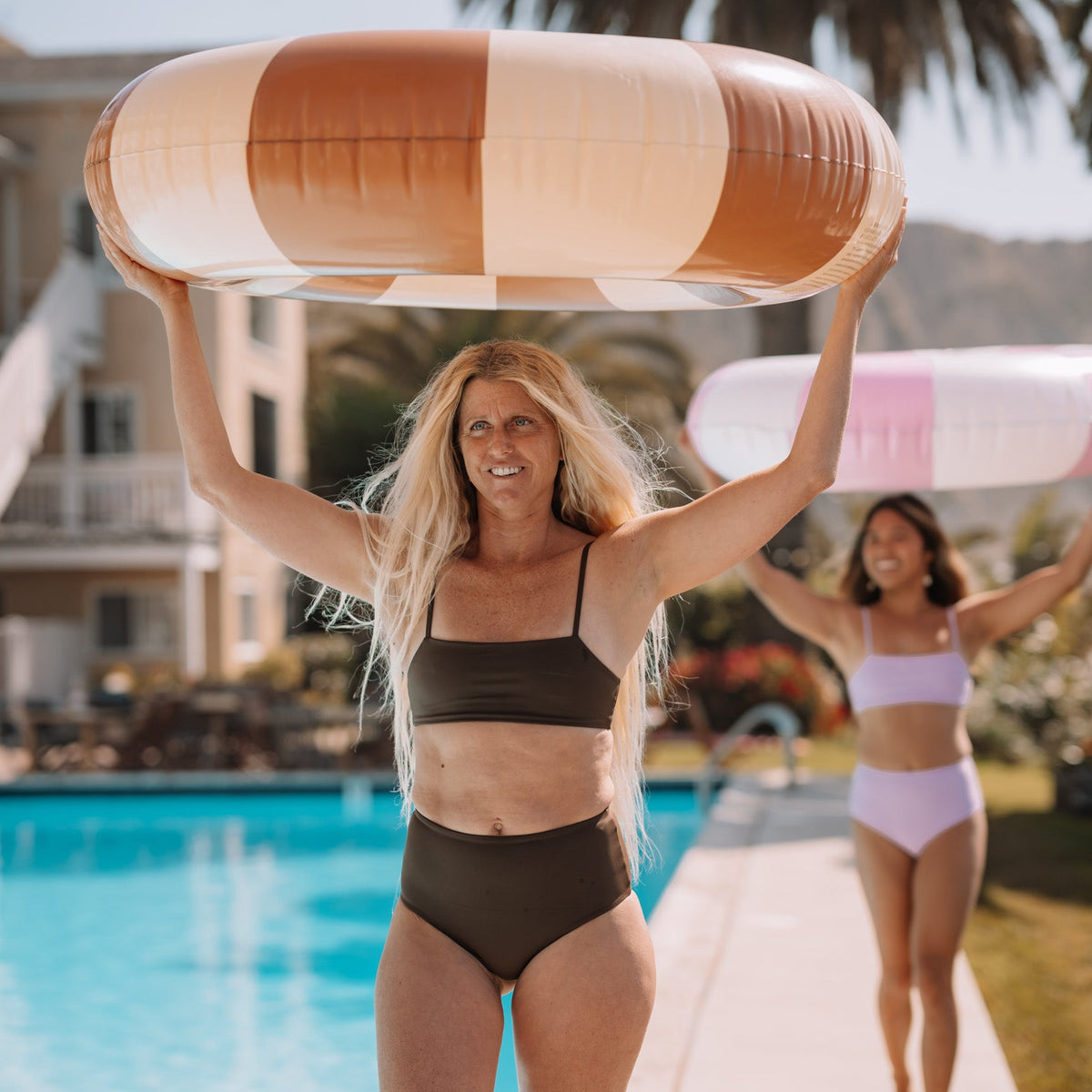 Woman holding a striped pool float by a pool with another person in the background.