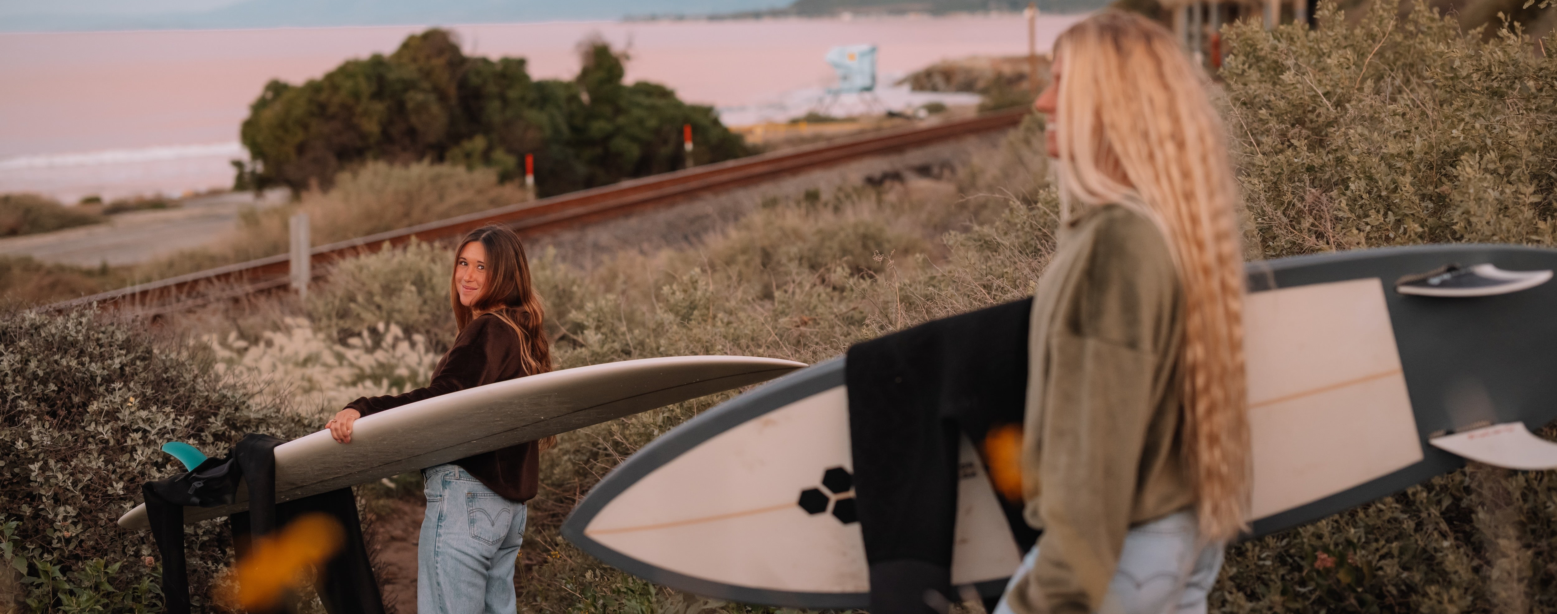 two people with surfboards near the train tracks