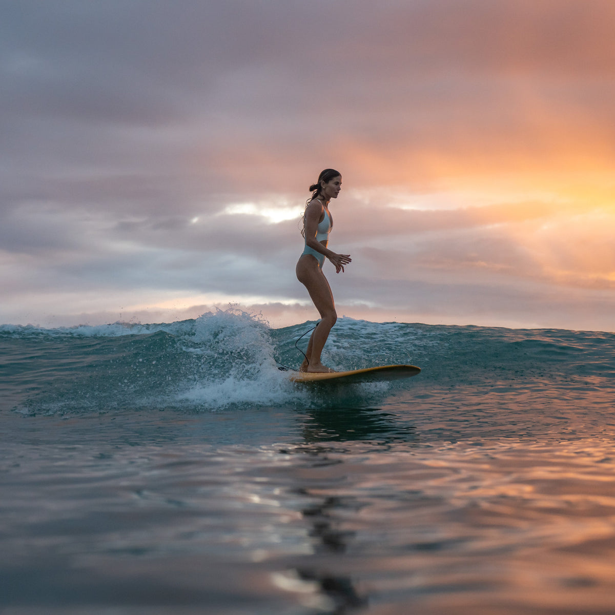 Person surfing on a wave with a colorful sunset sky