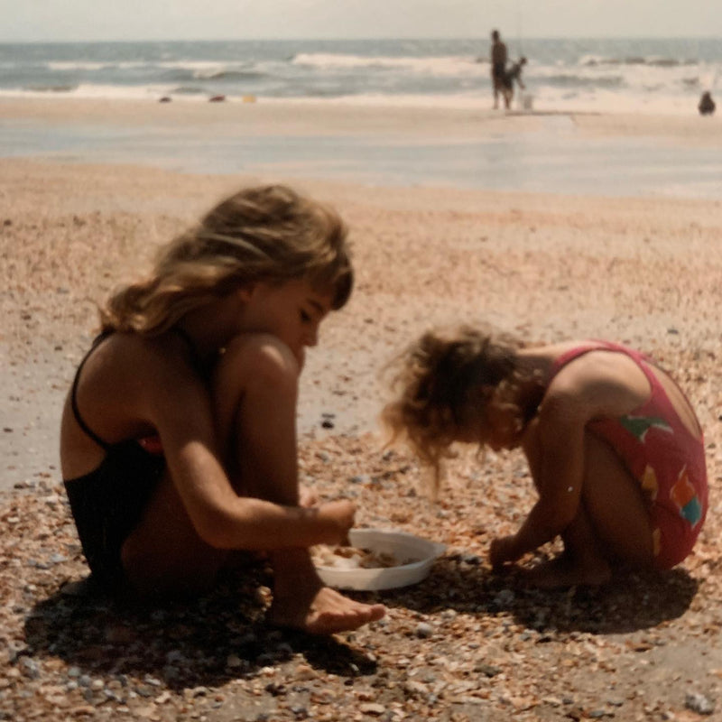 Two children playing on a sandy beach with the ocean in the background.