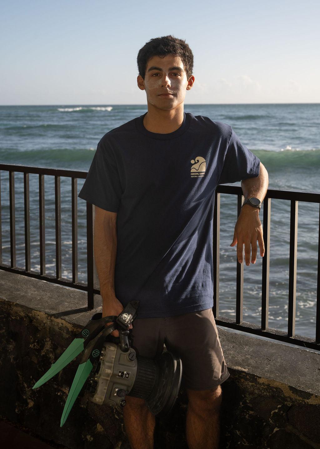 A person holding swim fins and water camera with ocean in background
