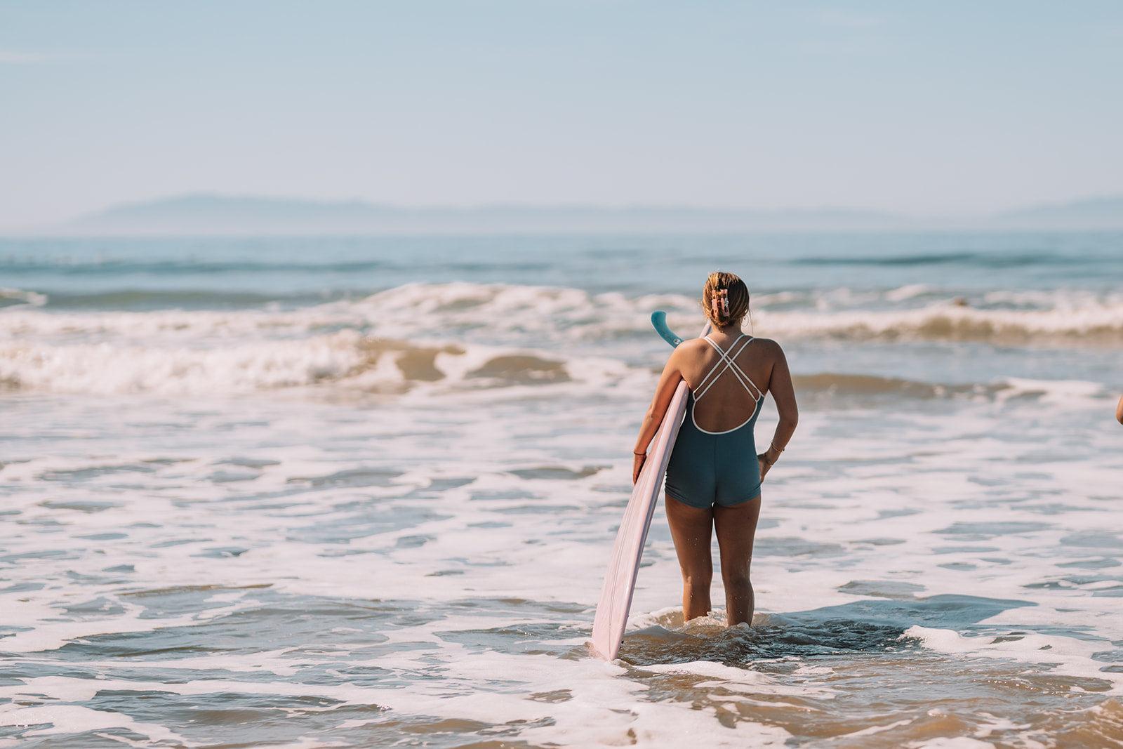 Woman holding a surfboard standing in shallow water at the beach